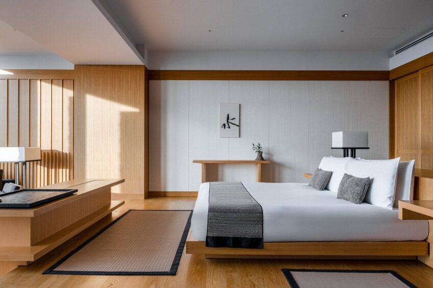 A serene Aman Tokyo hotel room featuring a minimalist Zen-inspired design with natural wood elements, tatami-style rugs, and soft, diffused lighting