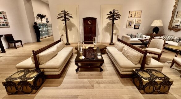 Elegant vintage furniture in a luxury auction setting, featuring two sofas, decorative trunks, a wooden coffee table, and striking palm tree sculptures.