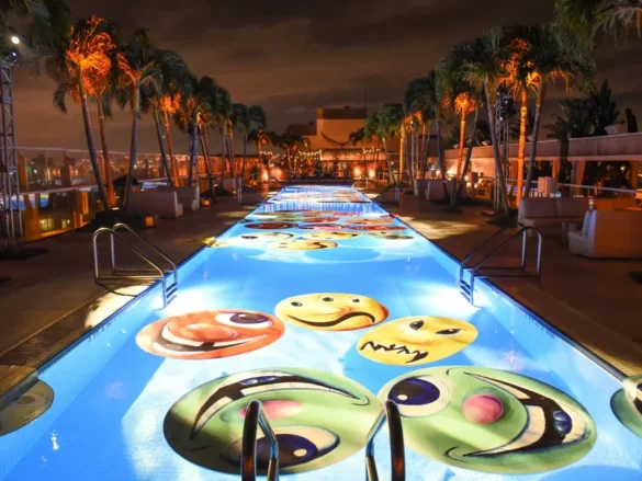 Art installation of colorful smiley faces projected onto a pool at night, surrounded by palm trees. Art Basel 24