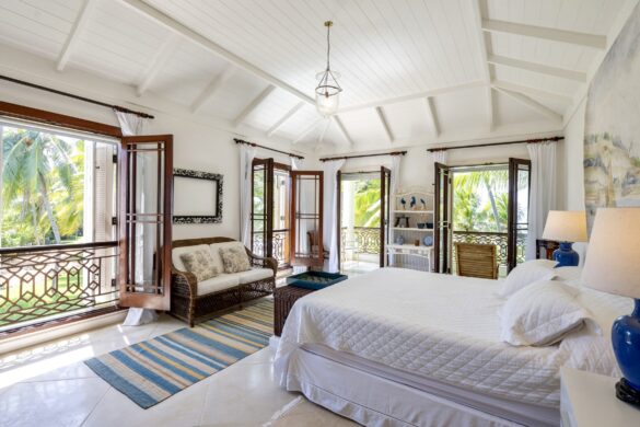 Bright, airy bedroom with vaulted ceiling, white linens, and French doors opening to veranda with ocean views