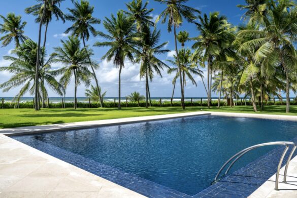 Collection of images showing the property's white colonial architecture, infinity pool, palm-lined gardens, elegant interiors with Moorish arches, and oceanfront views from various angle