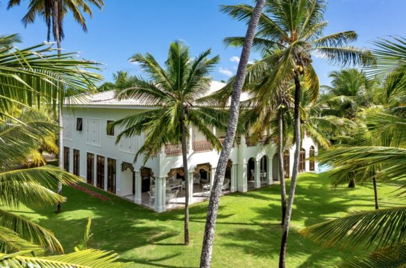 Collection of images showing the property's white colonial architecture, infinity pool, palm-lined gardens, elegant interiors with Moorish arches, and oceanfront views from various angle