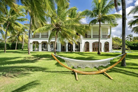 Collection of images showing the property's white colonial architecture, infinity pool, palm-lined gardens, elegant interiors with Moorish arches, and oceanfront views from various angle