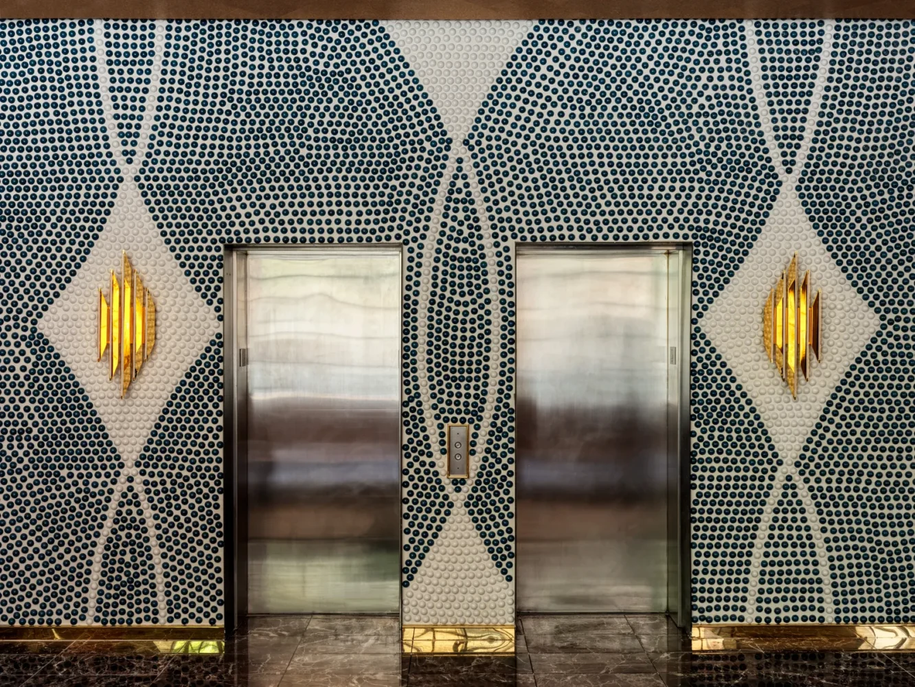 Luxury hotel elevator lobby with mosaic tile pattern, brushed steel elevator doors, and golden sconce lighting creating diamond motif