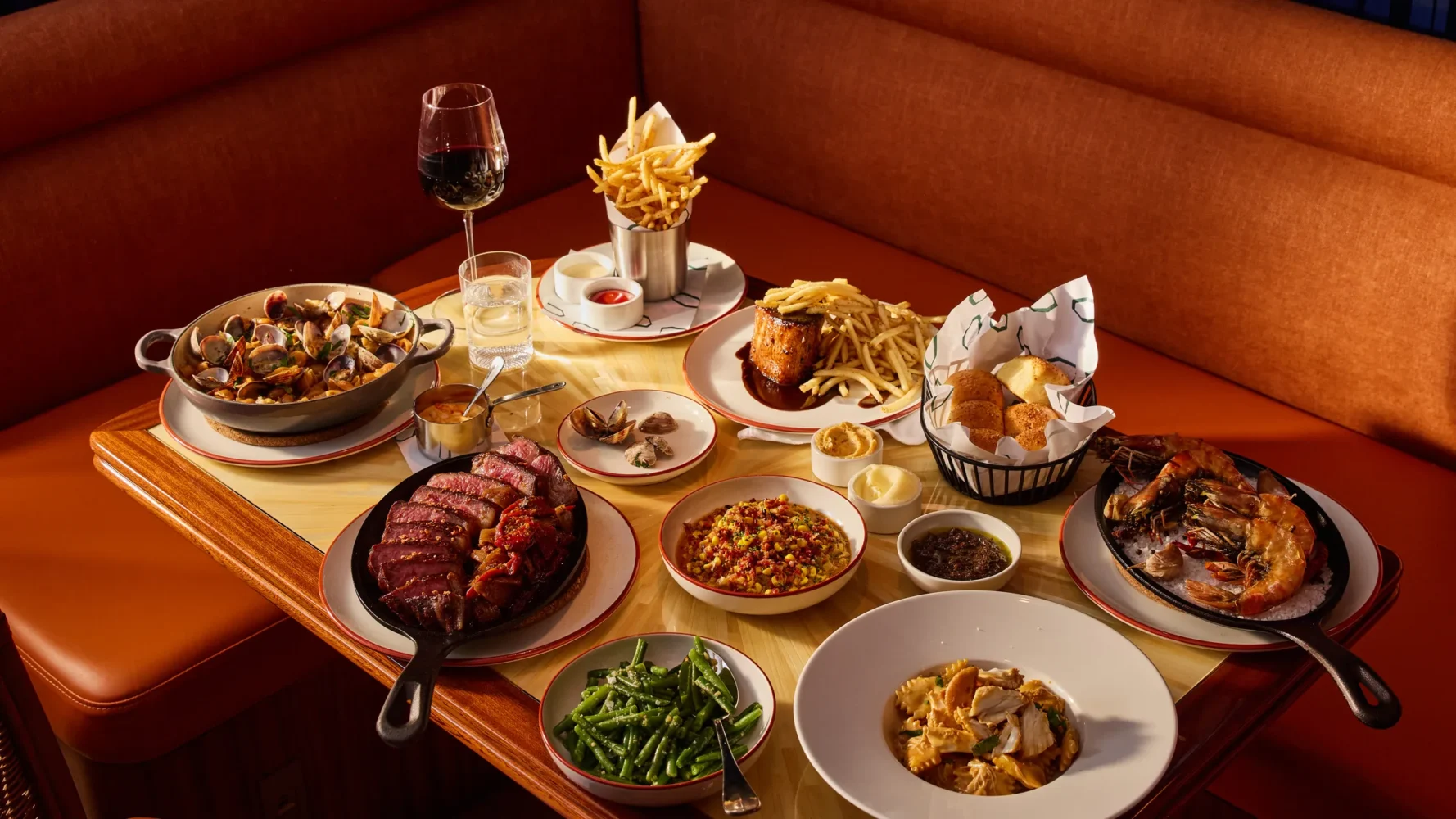 Luxury restaurant table setting with multiple dishes including steak, seafood, pasta, and sides on custom plateware